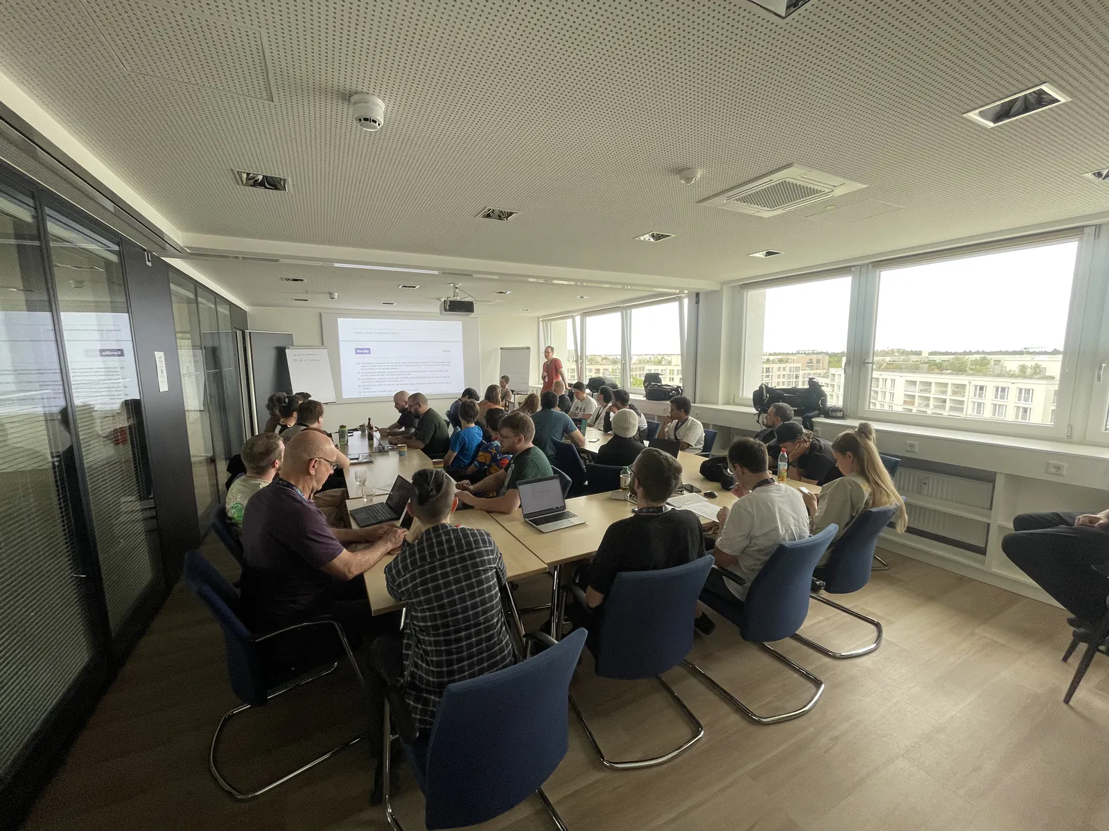 Attendees seated around a long table in a conference room, facing a projector screen.